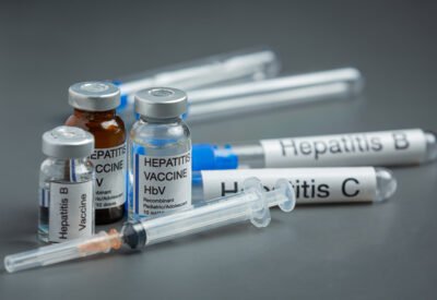 Seringas, vacinas e remédios contra a hepatite em cima de uma mesa cinza